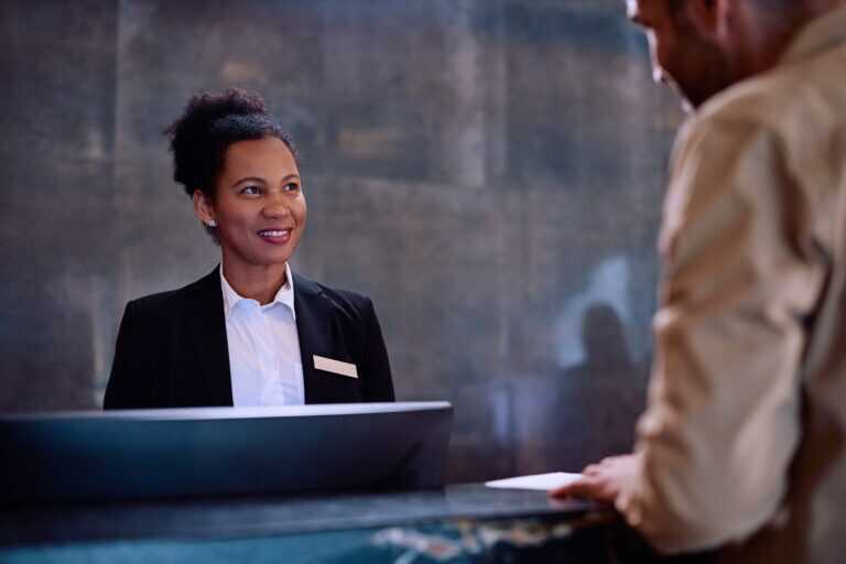 A hotel receptionist standing behind a front desk, interacting with a guest.