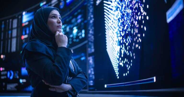 Portrait Of A Smart Focused Middle Eastern Software Engineer Analyzing Neural Network Big Data On A Digital Screen. Young Arab Woman In Hijab Working In An Innovative Internet Service Company