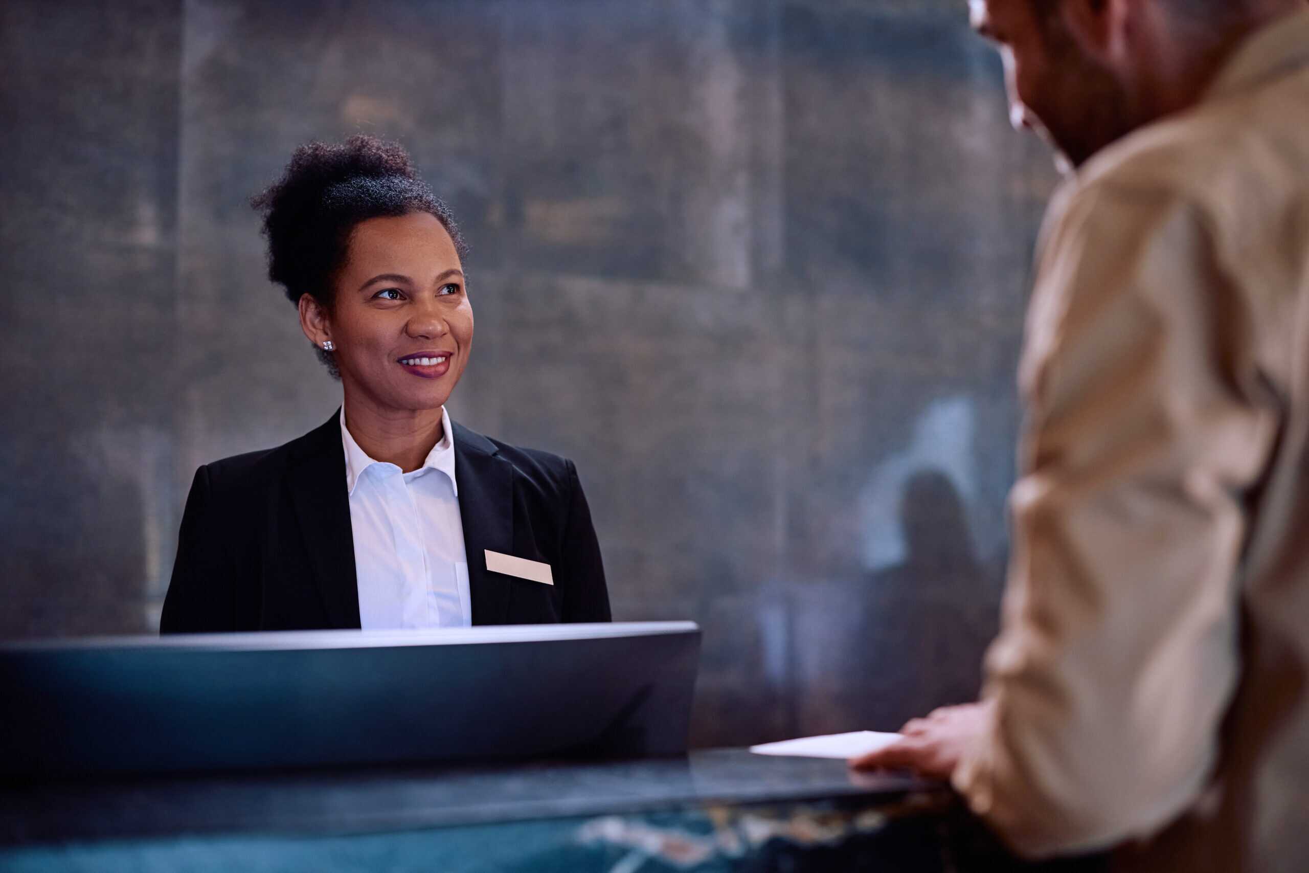 A hotel receptionist standing behind a front desk, interacting with a guest.