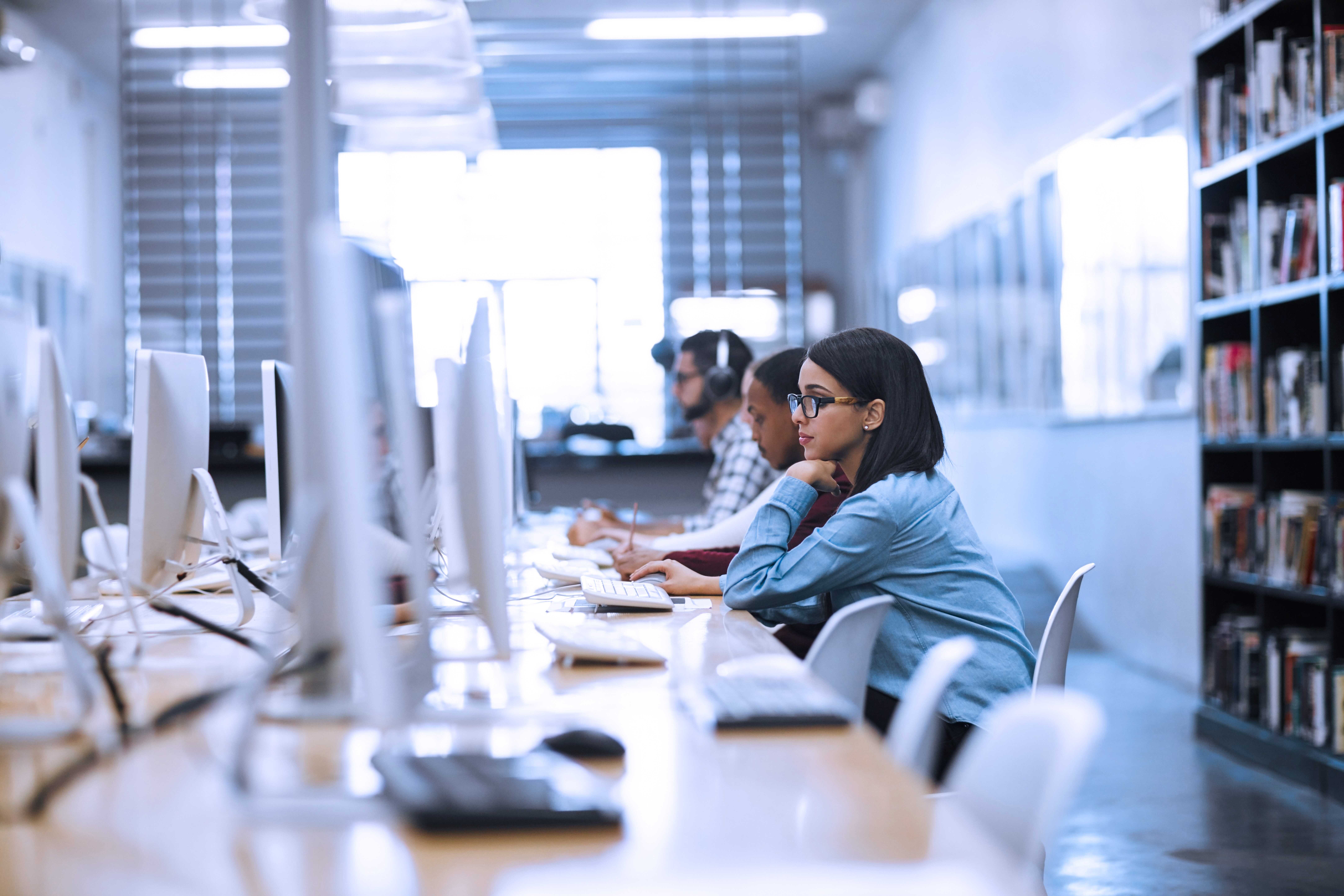Photograph of a modern computer lab with several people seated in a row using desktop computers.