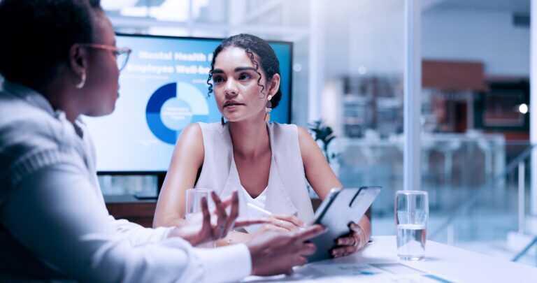 Woman holding a tablet deep in conversation with another woman.