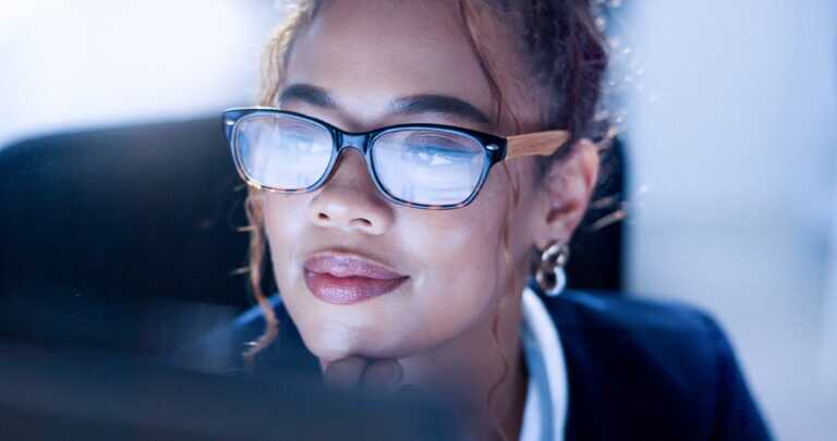 Woman wearing glasses reviewing documents on her computer.