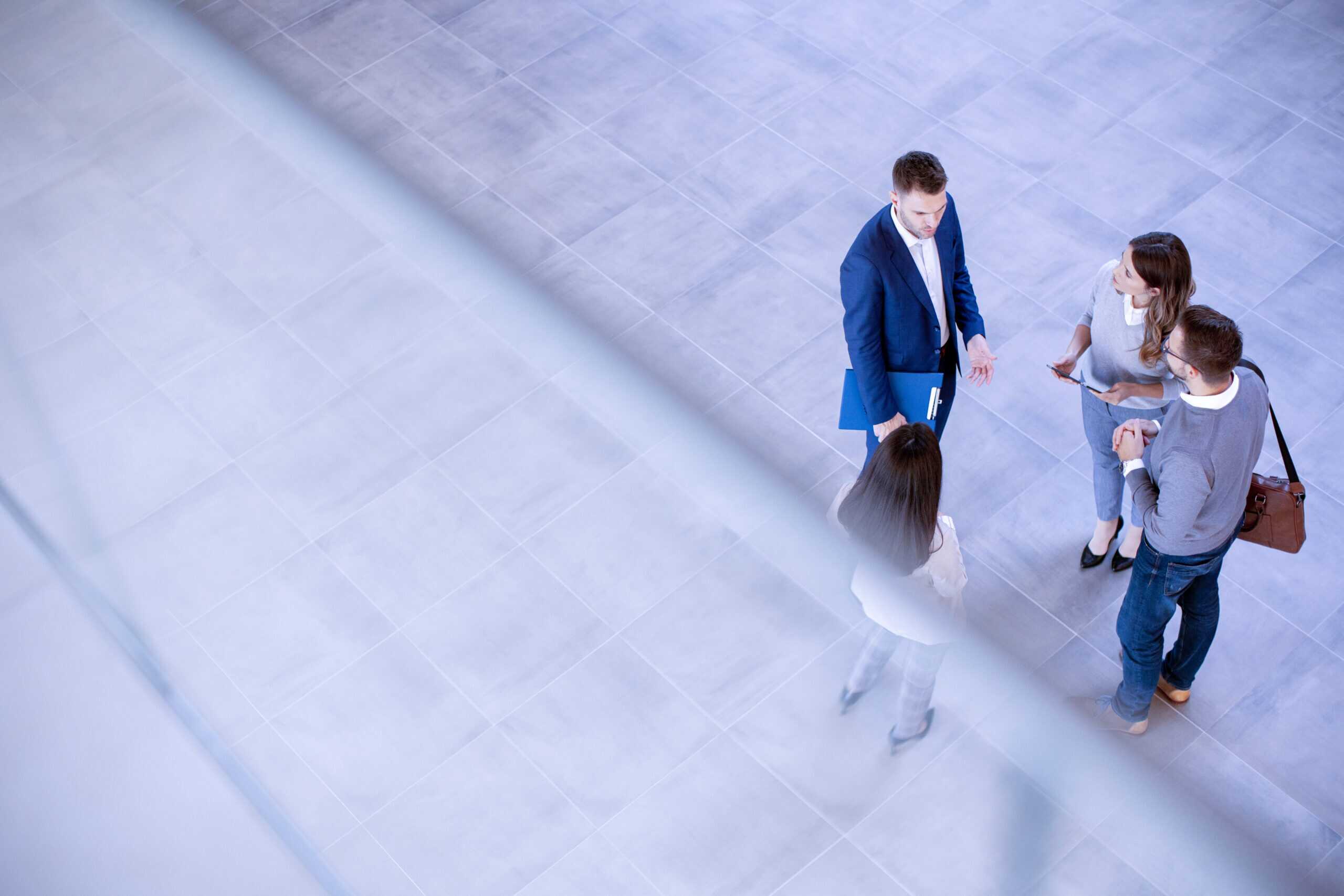 Four people standing in a tiled open space engaged in conversation, with two men and two women facing each other.